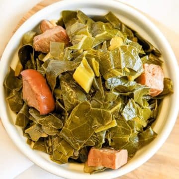 Slow cooker collards with ham in a small white dish on a wooden board (upclose)